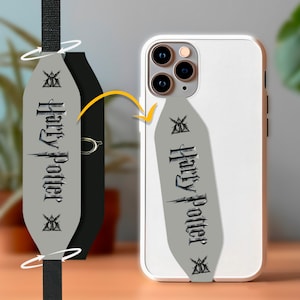 May include: A grey phone case with a black and white Harry Potter design. The case has a strap attached to the bottom.