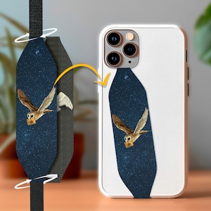 May include: A dark blue phone strap with a white owl carrying a letter against a starry night background. The strap is attached to a white phone case with a camera lens.