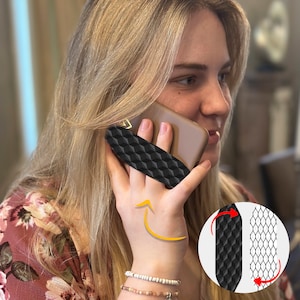 May include: A black phone grip with a geometric pattern is attached to a brown phone case. The grip is designed to be used with one finger to hold the phone securely.