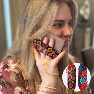 Op de afbeelding: Een telefoon grip met een kleurrijk bloemenpatroon. De grip wordt aan de achterkant van een telefoon bevestigd en zorgt voor een veiligere grip. De grip is gemaakt van een zacht, flexibel materiaal en is gemakkelijk aan te brengen en te verwijderen.