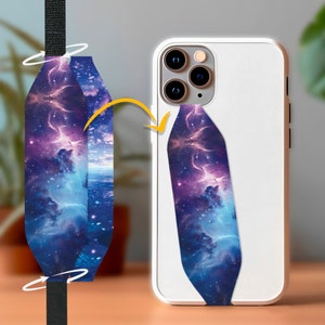May include: A phone strap with a galaxy print design. The strap is attached to a white phone case with a camera lens on the back.
