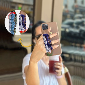 May include: A brown phone grip with a photo of a baseball team printed on it. The grip is attached to a light brown phone case.