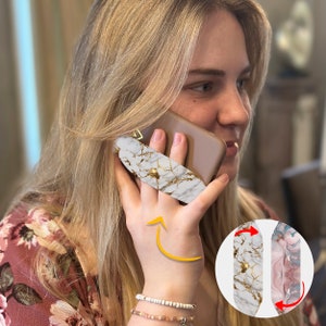 May include: White and gold marble phone grip attached to a phone. The grip has a curved shape and a gold metal ring. The image also shows a second phone grip with a pink and blue marble design.