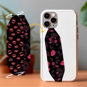 May include: A white phone case with a black and pink floral phone strap. The strap has a pattern of pink roses and leaves on a black background.