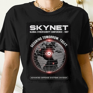 Könnte beinhalten: Schwarzes T-Shirt mit dem Text "SKYNET" und "GLOBAL CYBERSECURITY CONFERENCE - 1997". Das Design zeigt einen Globus mit rotem Auge und den Worten "SECURING TOMORROW. TODAY."