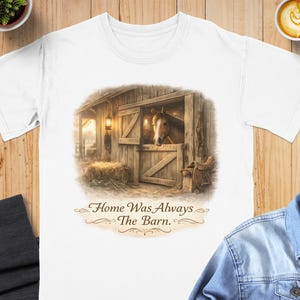 May include: White t-shirt featuring a detailed illustration of a horse in a barn. The artwork includes a horse head peeking out of a wooden stable door, with the text "Home Was Always The Barn." The design evokes a rustic, country theme.