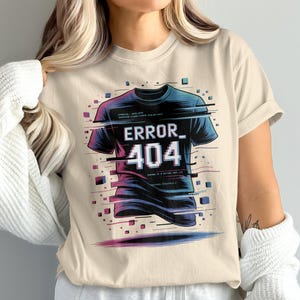 May include: Beige short-sleeved t-shirt with a graphic of a black t-shirt with the text "ERROR 404" in white. The graphic has a glitch effect with blue, purple, and pink accents. Small blue squares surround the graphic.