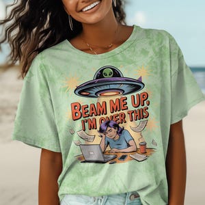 May include: Green tie-dye t-shirt with a cartoon illustration of a woman working on a laptop with a UFO above her. The text on the shirt reads "Beam me up, I'm over this."