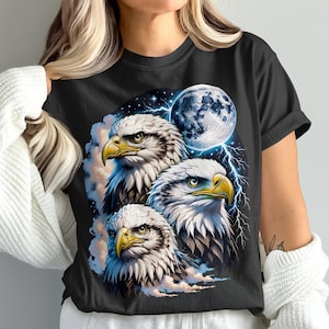 Puede incluir: Camiseta negra con un diseño de tres águilas calvas. Las águilas tienen plumas blancas y marrones, picos amarillos y ojos penetrantes. Una luna llena y rayos en el fondo crean una escena dramática. Las águilas se destacan sobre un cielo nublado.