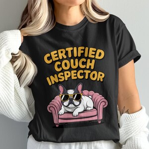 Könnte beinhalten: Schwarzes T-Shirt mit dem Text "CERTIFIED COUCH INSPECTOR" in Gelb und Orange. Ein Cartoon-Französisch Bulldogge mit Sonnenbrille liegt auf einer rosa Couch. Dies ist ein Freizeitkleidungsstück.
