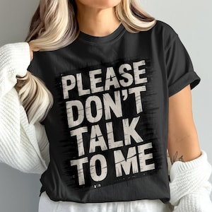 Puede incluir: Camiseta negra con la frase "PLEASE DON'T TALK TO ME" en una fuente blanquecina desgastada. El texto está dentro de un rectángulo negro con un borde texturizado. Una prenda informal para el uso diario.