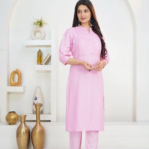 May include: A light pink long-sleeved tunic with a mandarin collar, a button-down placket with vertical pleats, and white floral embroidery on the sleeves, paired with matching light pink straight-leg trousers. The text HodgePodgeYarn is visible.