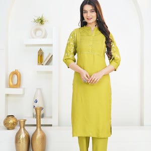 May include: A lime green kurta set featuring a straight-cut tunic with a pleated bodice, three-quarter sleeves with white embroidery, and a mandarin collar. The set includes matching straight-leg trousers and is labeled with the text HodgePodgeYarn.