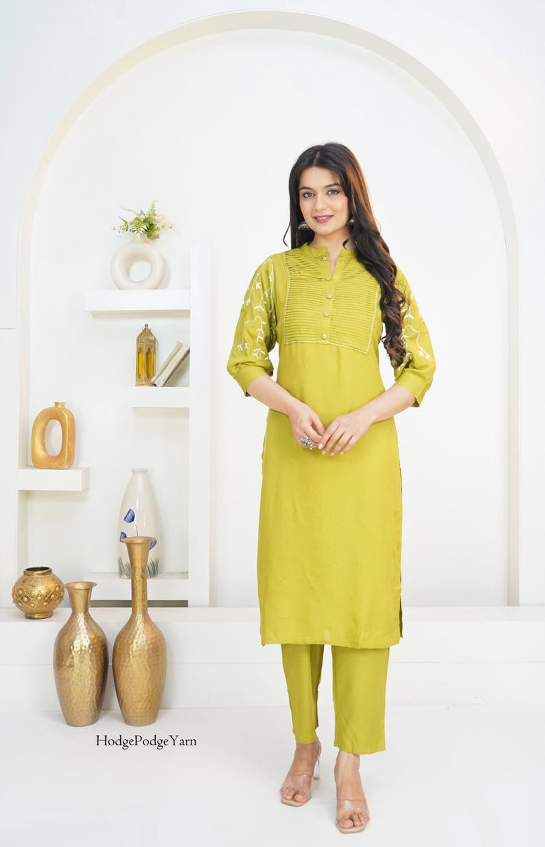 May include: A lime green kurta set featuring a straight-cut tunic with a pleated bodice, three-quarter sleeves with white embroidery, and a mandarin collar. The set includes matching straight-leg trousers and is labeled with the text HodgePodgeYarn.