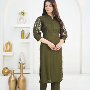 May include: An olive green kurta set featuring a long-sleeved tunic with a pleated bodice, button-down front, and white floral embroidery on the sleeves, paired with matching straight-leg trousers. The text HodgePodgeYarn is visible at the bottom.
