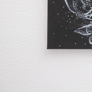 Pode incluir: Uma pintura em tela preta com desenhos abstratos brancos e cinzentos. A pintura est&aacute; em uma parede branca.