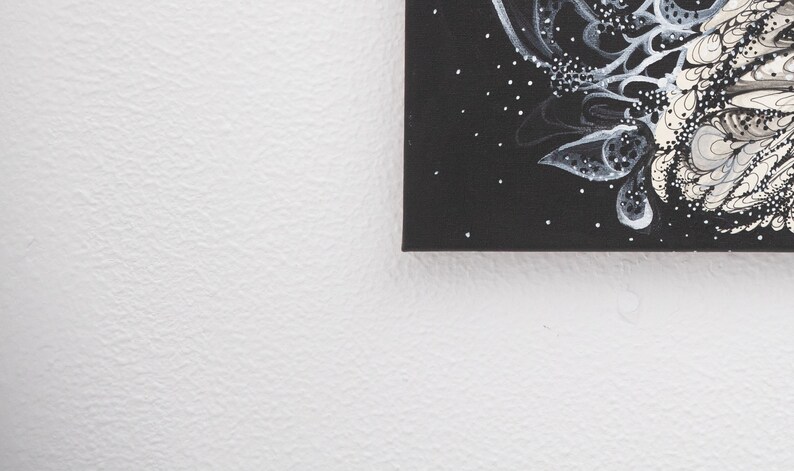 Pode incluir: Uma pintura em tela preta com desenhos abstratos brancos e cinzentos. A pintura est&aacute; em uma parede branca.