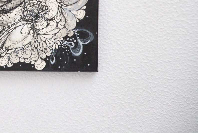 Pode incluir: Uma pintura em tela preta com desenhos abstratos brancos e cinzentos. A pintura &eacute; emoldurada e pendurada em uma parede branca.