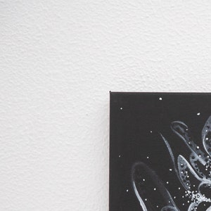 Pode incluir: Uma pintura em tela preta com desenhos abstratos brancos. O desenho apresenta formas e pontos em espiral.