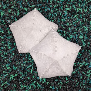 May include: Two white, star-shaped, decorative pillows with a textured surface. The pillows are on a black and green background.