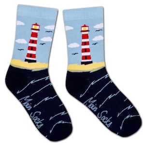 Könnte beinhalten: Paar Crew-Socken mit Leuchtturm-Design. Die Socken haben einen hellblauen Himmel mit weißen Wolken und schwarzen Vögeln. Der Leuchtturm ist rot und weiß, auf gelbem Sand, mit dunkelblauen Wellen am unteren Rand. Der Text "Main Socks" ist seitlich aufgedruckt.