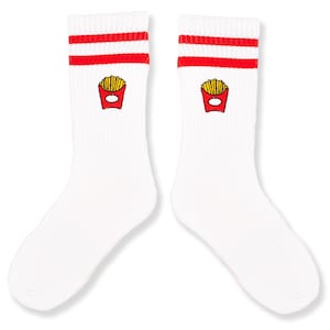 Könnte beinhalten: Paar weiße Sportsocken mit roten Streifen am oberen Rand. Jede Socke hat ein kleines gesticktes Bild eines roten Pommes-Containers, gefüllt mit gelben Pommes. Die Socken sind aus weichem, geripptem Material.