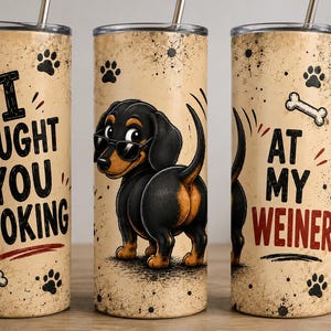 Peut inclure: Un gobelet cylindrique en acier inoxydable avec un fond beige vieilli, orné d'empreintes de pattes noires et d'os blancs. Le texte indique I CAUGHT YOU LOOKING AT MY WEINER. Un teckel noir et feu portant des lunettes de soleil est au centre.