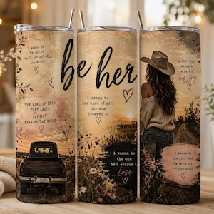 Peut inclure: Un gobelet cylindrique en métal orné d'un paysage de coucher de soleil rustique, d'un pick-up vintage et d'une personne portant un chapeau de cowboy. Le design inclut le texte 'be her' et diverses phrases romantiques avec des cœurs.