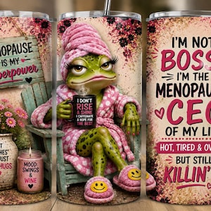 May include: A cylindrical tumbler featuring a green frog wearing a pink bathrobe, towel, and smiley face slippers. The design includes text: Menopause is my superpower, I don't rise and shine, I caffeinate, and I'm not bossy, I'm the menopausal CEO.