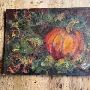 May include: An oil painting on canvas featuring a large, vibrant orange pumpkin surrounded by dark green and brown foliage. The artwork displays textured brushstrokes and includes the signature Gale Cooper in the bottom right corner of the piece.