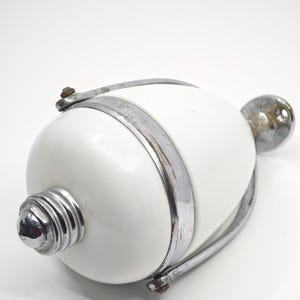 Könnte beinhalten: Ein weißes, eiförmiges Objekt mit einem silbernen Metallband und Akzenten. Das Objekt hat einen abgerundeten silbernen Knopf an einem Ende und einen geriffelten silbernen Sockel am anderen. Das Metall weist Gebrauchsspuren auf.