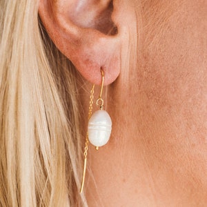 May include: A pair of gold earrings with a single white pearl dangling from each earring.
