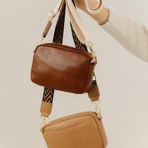 May include: Two leather crossbody bags with adjustable straps. The top bag is brown and the bottom bag is tan.