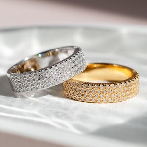 May include: Two diamond wedding bands, one in silver and one in gold, on a white surface.
