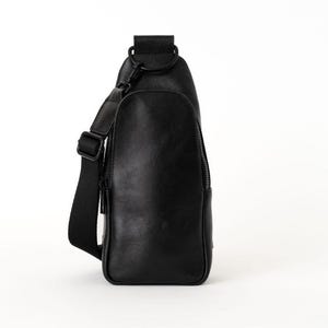 May include: A black sling bag with a single adjustable shoulder strap. The bag has a zippered front pocket and a top handle. The bag is made of a smooth, leather-like material and is designed to be worn across the body.