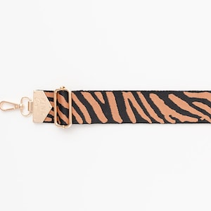 May include: A black and brown zebra print adjustable strap with a gold metal clasp and hook.