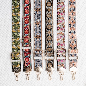 May include: Six patterned bag straps with gold-coloured metal fixings. The straps display floral and geometric designs in a range of colours, including green, red, blue, black, pink, and brown. Each strap has a clasp and adjustable buckle.