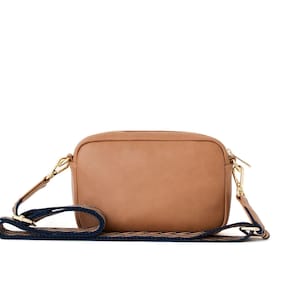 May include: A tan leather camera bag with a navy blue and white patterned strap.
