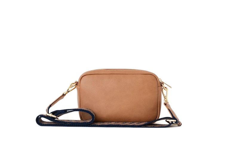 May include: A tan leather camera bag with a navy blue and white patterned strap.