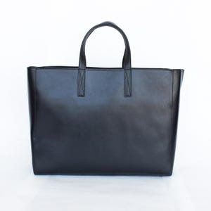 May include: A black tote bag with two handles and a rectangular shape. The bag is made of a smooth material and has a simple, minimalist design. The handles are attached to the bag with reinforced stitching.