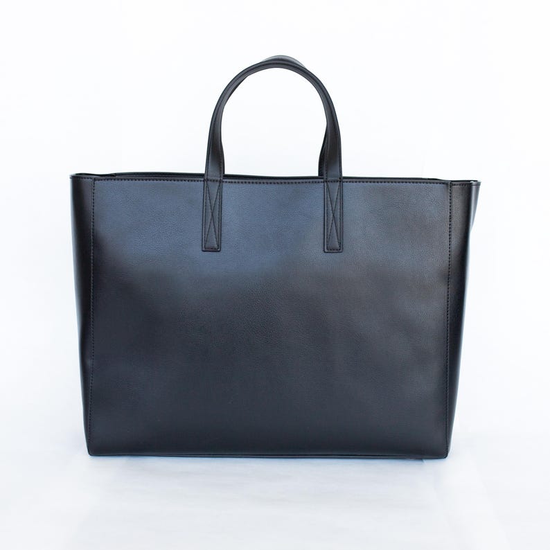 May include: A black tote bag with two handles and a rectangular shape. The bag is made of a smooth material and has a simple, minimalist design. The handles are attached to the bag with reinforced stitching.