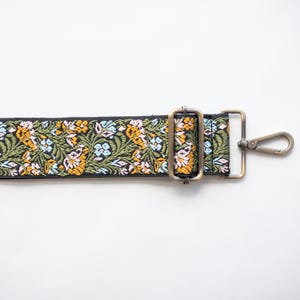 May include: A black floral patterned strap with a metal clasp and buckle. The strap features a repeating pattern of yellow, pink, blue, and green flowers and leaves. The metal hardware has a bronze finish.