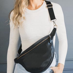 May include: Black leather crossbody bag with a gold zipper and adjustable black strap. The bag is worn across the body. The bag is a crescent shape and has a gold zipper.