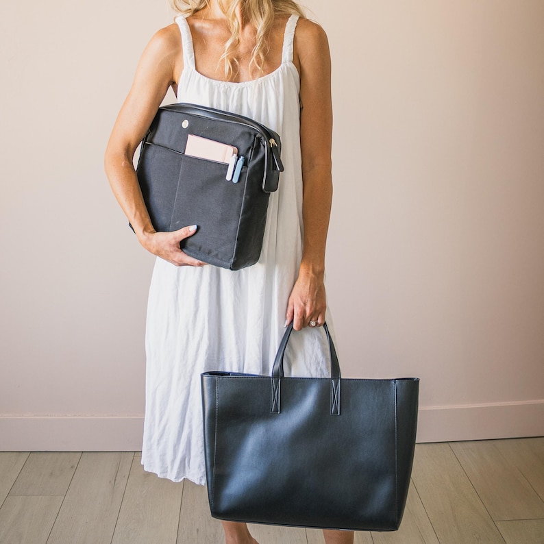 May include: Two black handbags. One is a rectangular messenger bag with a front pocket and a light blue zipper pull. The other is a large, rectangular tote bag with two handles.