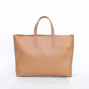 May include: A tan leather tote bag with two top handles and a rectangular shape. The bag has a simple, minimalist design and is suitable for everyday use. The bag is made of a smooth, solid material.