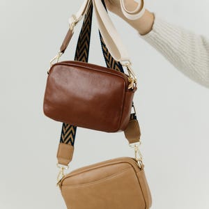 May include: Two leather crossbody bags with adjustable straps. The top bag is brown and the bottom bag is tan.
