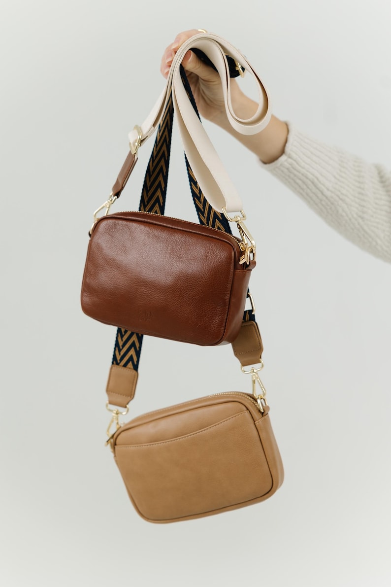 May include: Two leather crossbody bags with adjustable straps. The top bag is brown and the bottom bag is tan.