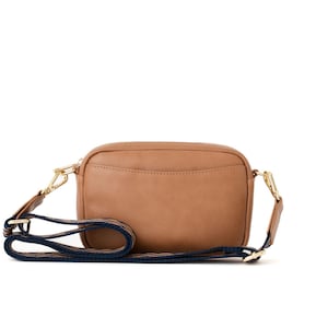 May include: A brown leather crossbody bag with a navy blue and white striped strap.