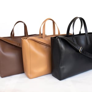 May include: Three leather tote bags in shades of brown and black. The bags have top handles and a rectangular shape. The black bag has a shoulder strap. The bags are displayed against a white background.