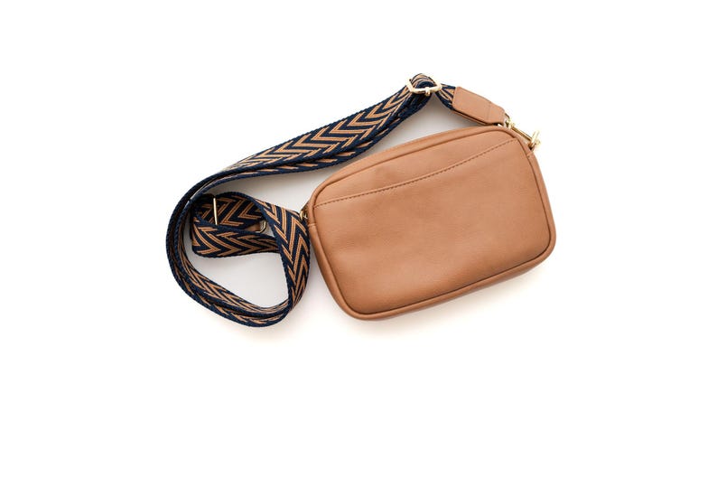 May include: A brown leather crossbody bag with a black and brown chevron patterned strap.